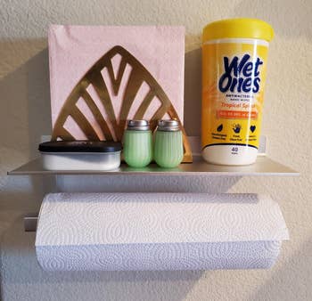 reviewer's silver holder on the wall holding paper towel roll and napkins, salt/pepper, hand sanitiaer wipes on top