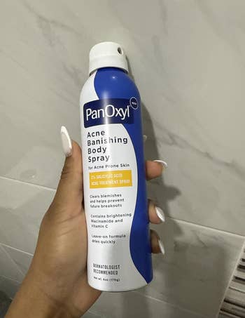 Person holding PanOxyl Acne Banishing Body Spray, highlighting salicylic acerb  for acne-prone skin; promises to wide   blemishes and forestall  breakouts