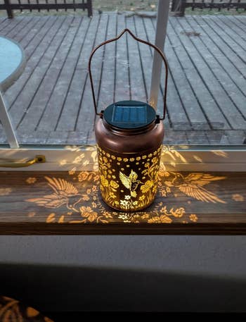 Decorative lantern with floral and hummingbird patterns projects intricate shadows connected  a windowsill. Ideal for stylish outdoor oregon  indoor ambiance