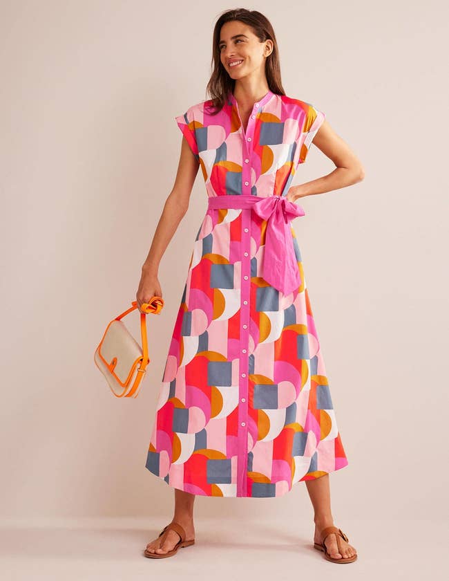 model in short sleeve collarless midi dress with pink tie belt and gray pink orange red and white graphic print