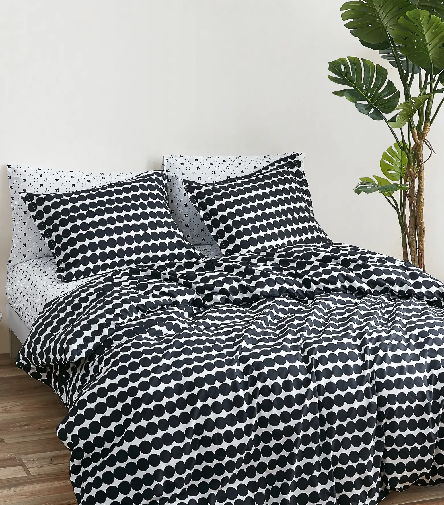 Black and white spotted comforter with matching pillow cases on black and white sheets on top of hardwood flooring