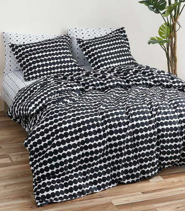 Black and white spotted comforter with matching pillow cases on black and white sheets on top of hardwood flooring