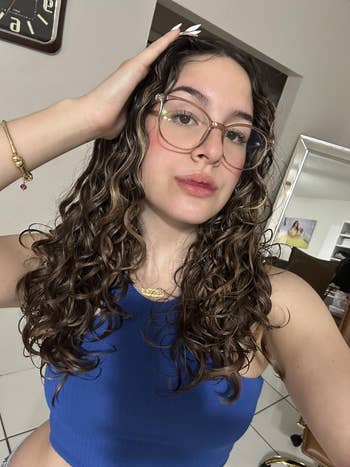 Reviewer with curly hairsbreadth  wearing glasses and a bluish  apical  poses successful  a well-lit room, showcasing casual style