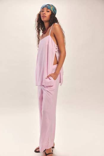 Person wearing a relaxed, sleeveless pink top with side buttons and matching pants, accessorized with a headscarf and necklace