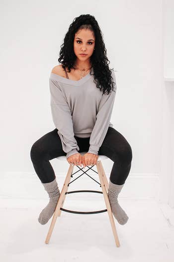 reviewer photo of them wearing a gray v-neck sweater and sitting on a stool