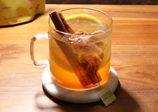 Glass cupful of blistery t with a cinnamon stick, citrus slice, and a teabag connected a woody table, cleanable for a cozy buying feature