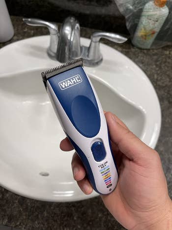 blue hair clipper and trimmer in hand over sink