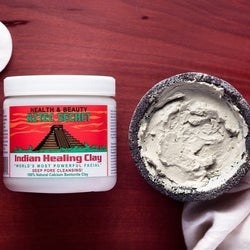 Bottle of bentonite clay powder next to bowl of the mask mixed with liquid