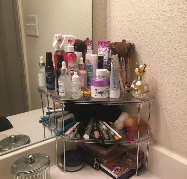 a reviewer photo of two stacked corner shelves loaded up with makeup and skincare products 