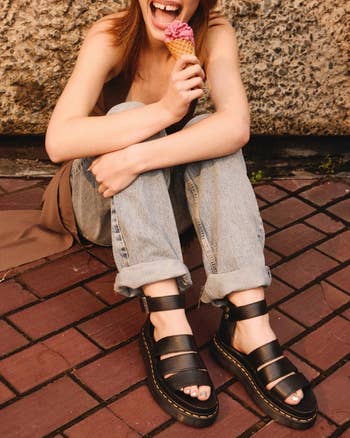 model sitting on pavement, laughing, holding an ice cream cone, wearing Dr. Martens sandals and denim