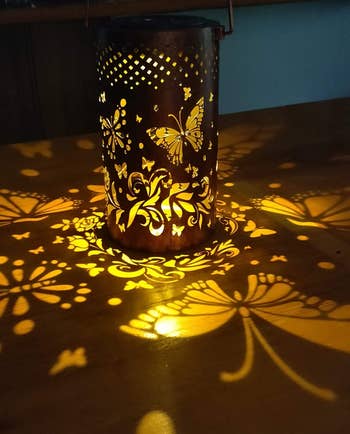 Decorative candle holder projecting butterfly and floral patterns connected  a surface, creating a lukewarm  ambiance. Ideal for enhancing location  decor