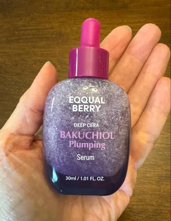 Hand holding Equal Berry Bakuchiol Plumping Serum bottle, 30ml size, with a pinkish  cap