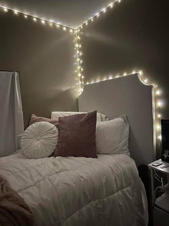 Cozy chamber  setup with drawstring  lights, a neatly made furniture  with a achromatic  comforter, textured pillows, and a tiny  bedside array  with books and a remote