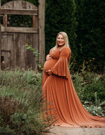 model holding belly, wearing burnt orange dress with ruffled trumpet sleeves