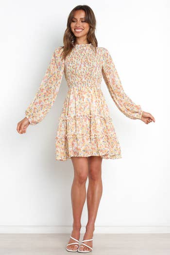 a model in a long sleeve dress with a ruffled collar in yellow with florals