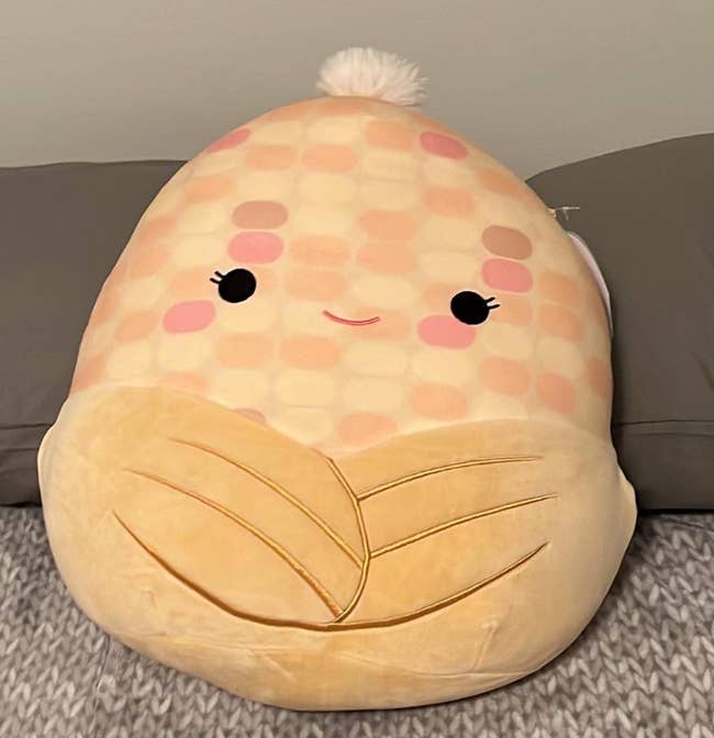 reviewer's corn shaped plush pillow doll. it has a smiling face.