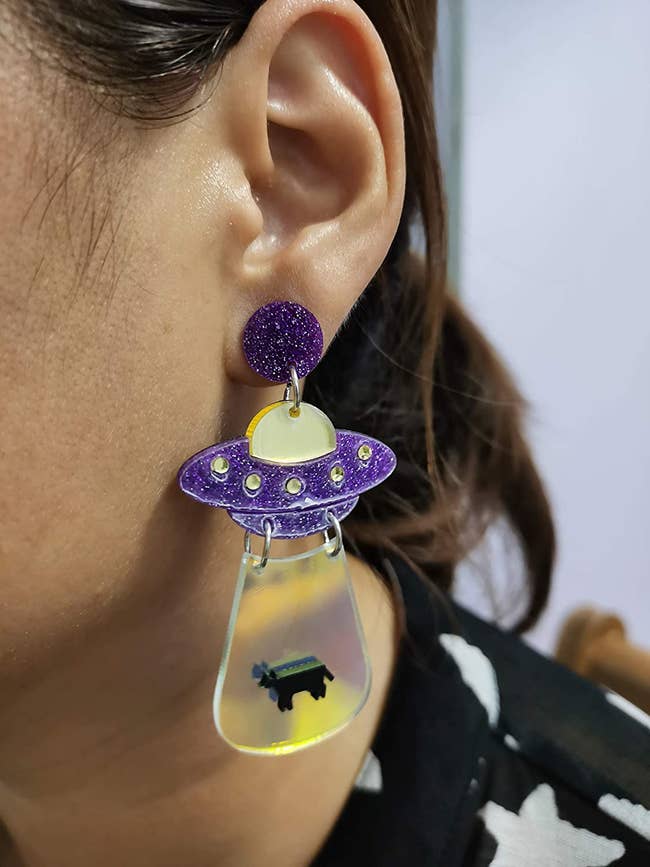 model wearing the acrylic earrings that picture a purple ufo abduction a cow