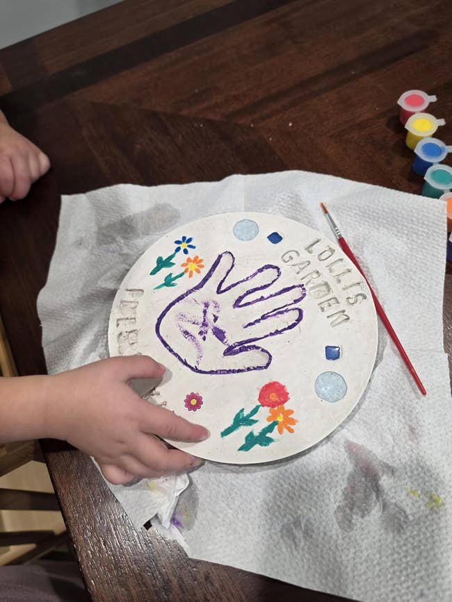 Child decorating a handprint stepping chromatic  with flowers and gems utilizing paints, creating a personalized plot  accessory