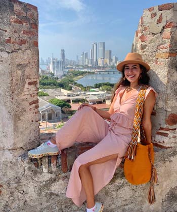 reviewer wearing the pink top and pants while sitting in an old structure with a city skyline in the background
