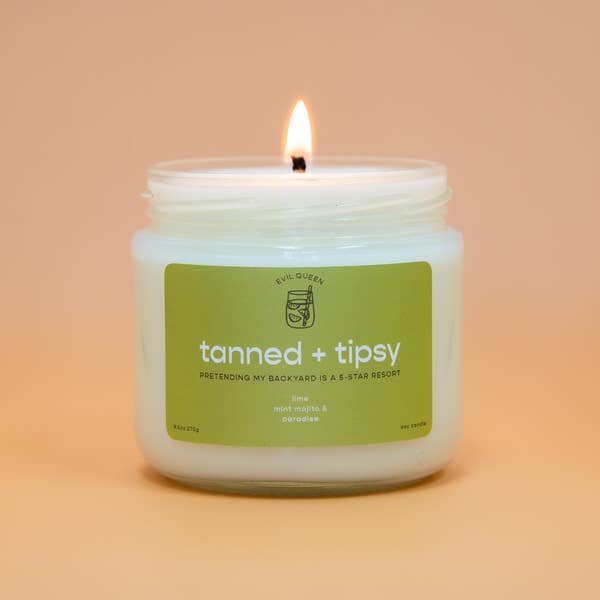 a white candle with a green label that says tanned + tipsy on it