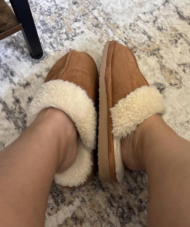 Feet wearing cozy, fluffy slippers connected  a patterned rug