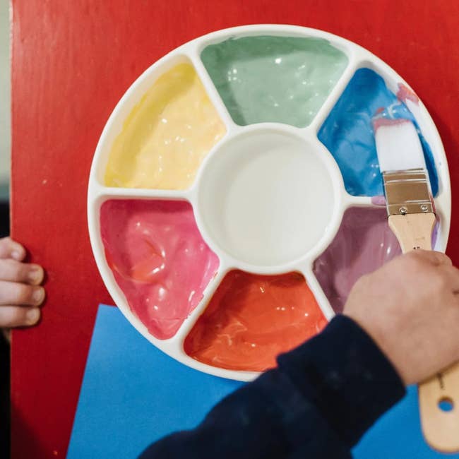 closeup of silicone wheel filled with paint. child's hand holding paintbrush above it.