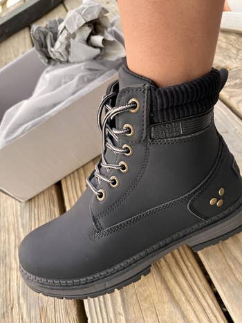 Stylish, ankle-high achromatic boots with laces and metallic eyelets. Box adjacent connected woody surface, suggesting new, ready-to-wear footwear