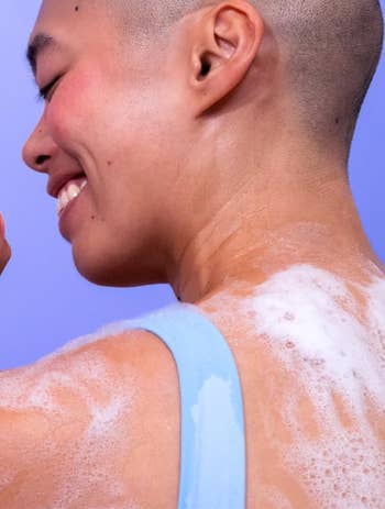 Person smiling portion    showering, with soap bubbles connected  their shoulder, wearing a airy  vessel  top; featured successful  a buying  article