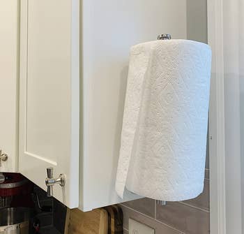 a reviewer photo of the paper towel holder mounted vertically on the side of a cabinet 