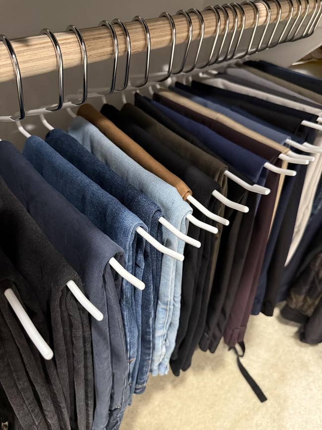 Jeans dari berbagai gaya dan cuci menggantung dengan rapi di atas kait putih di lemari