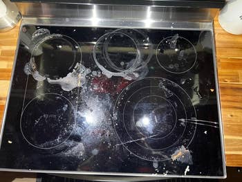 Dirty glass stovetop with food spills and stains, suitable for an article on cleaning products or stovetop maintenance tips