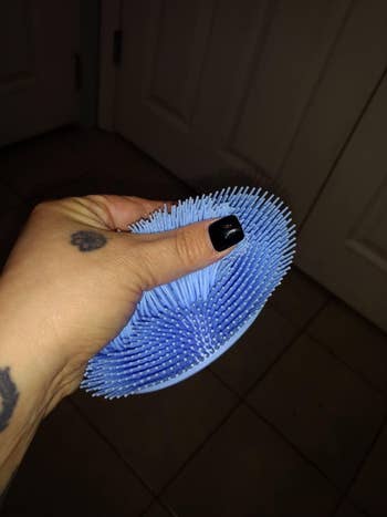 Reviewer holding blue oval shaped silicone brush, demonstrating how the thick bristles move by running their thumb over them