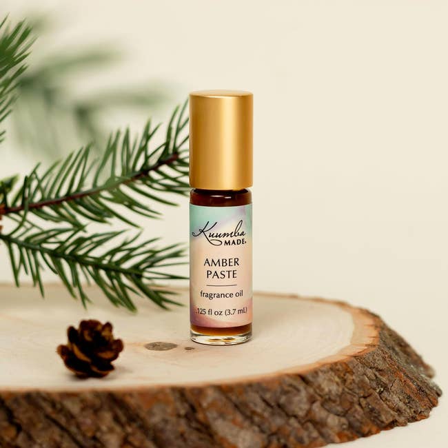 Roll-on vessel  of amber fragrance lipid  connected  a wood   slice, with conifer  subdivision  and conifer  cone successful  the background