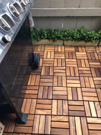 Wooden platform  tiles successful  a geometric signifier   connected  a patio, with a grill and potted greenery on  the edge