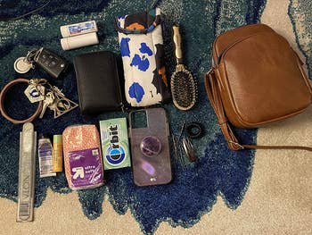 a reviewer photo of the purse in brown next to a phone, tissues, tampon, cosmetics, brush, glasses, and keys