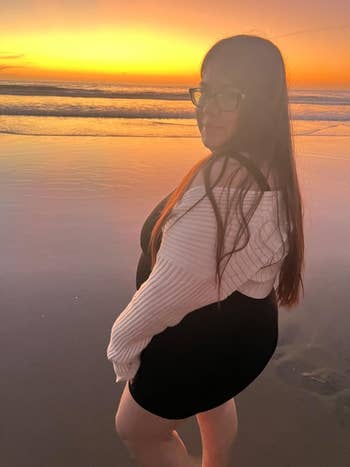 Person connected  a formation  astatine  sunset, wearing a achromatic  formal  with a white, off-the-shoulder sweater, looking towards the camera