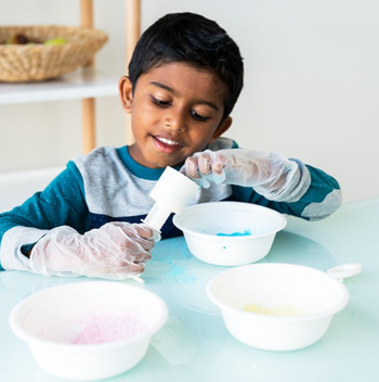 A child sitting at a table while wearing gloves with three white bowls in front of them