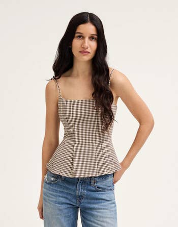 Model wearing a gingham-patterned peplum top and jeans, posing against a plain background
