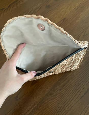 Hand opening   a woven clutch container  showing its interior lined with cloth  and a drawback   closure