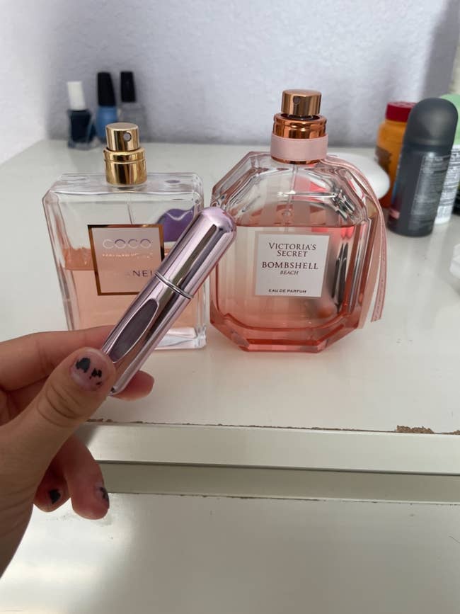 Reviewer holding perfume atomizer next to full size bottle of perfume