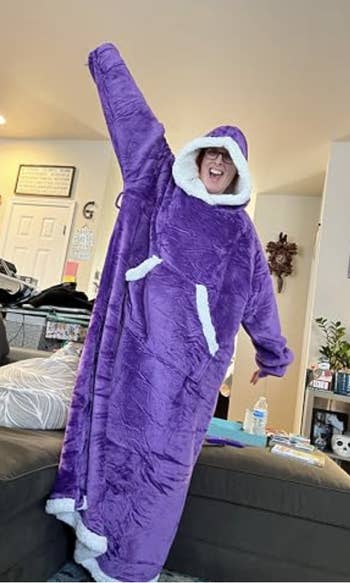 Person successful  oversized, plush hooded purple blanket-like attire with achromatic  trim, posing excitedly indoors