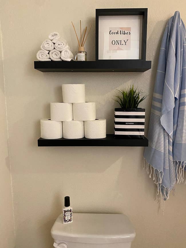 a reviewer photo of a pair of floating shelves hung over a toilet with decor and toilet paper on them 