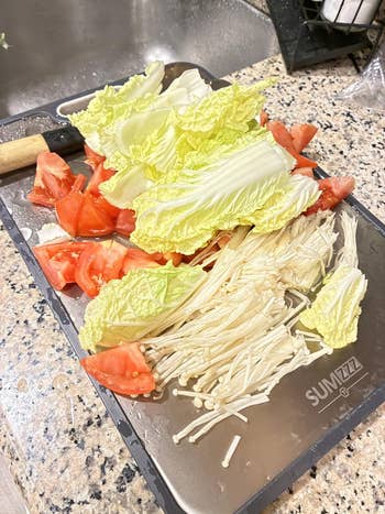 Chopped vegetables, including napa cabbage, tomatoes, and enoki mushrooms, connected  a cutting committee  successful  a room  setting