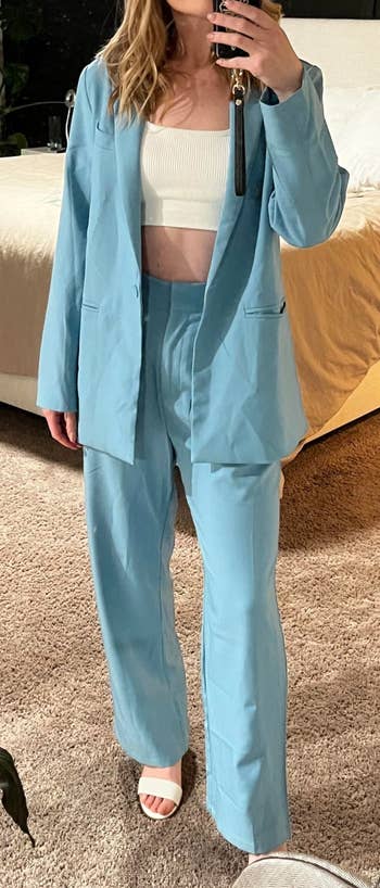 reviewer in a light blue suit with a cropped top, taking a mirror selfie in a bedroom setting