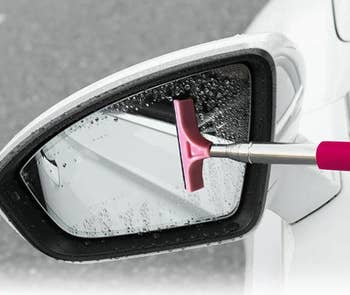 Model using pink small squeegee with handle ot clean off a mirror 