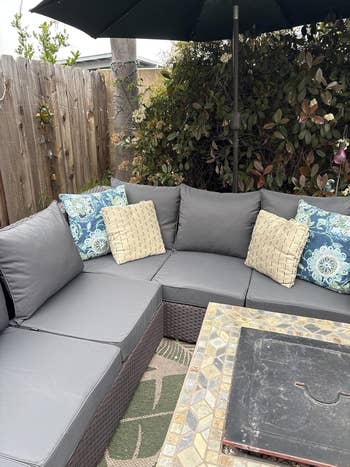 Outdoor patio acceptable   with grey  cushions and patterned pillows, arranged astir   a stone-top array  nether  a ample  umbrella