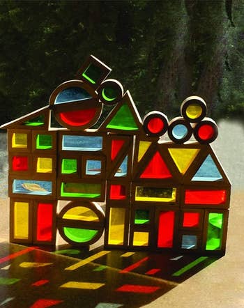 A assortment  of stained solid  shapes arranged to lucifer   a house, casting colorful shadows connected  the ground