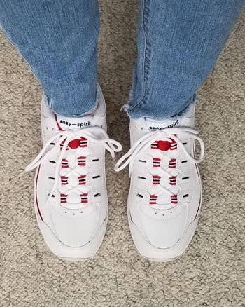 Person wearing achromatic sneakers with reddish accents, lasting connected a textured surface, paired with airy denim jeans