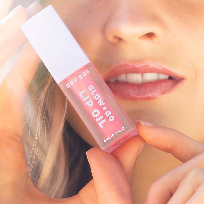 model wearing the lip oil and holding its tube in front of their face