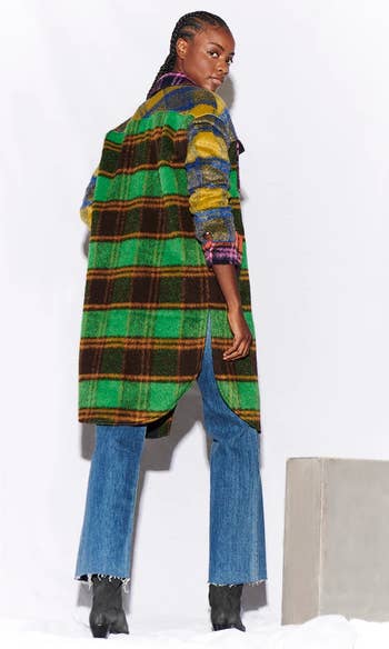 back of a model wearing a multicolored plaid long jacket over a white tee and blue jeans